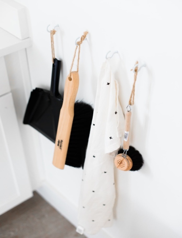A Dust Pan, Brush, and Cloth Hanging Off Hooks Attached to a Wall